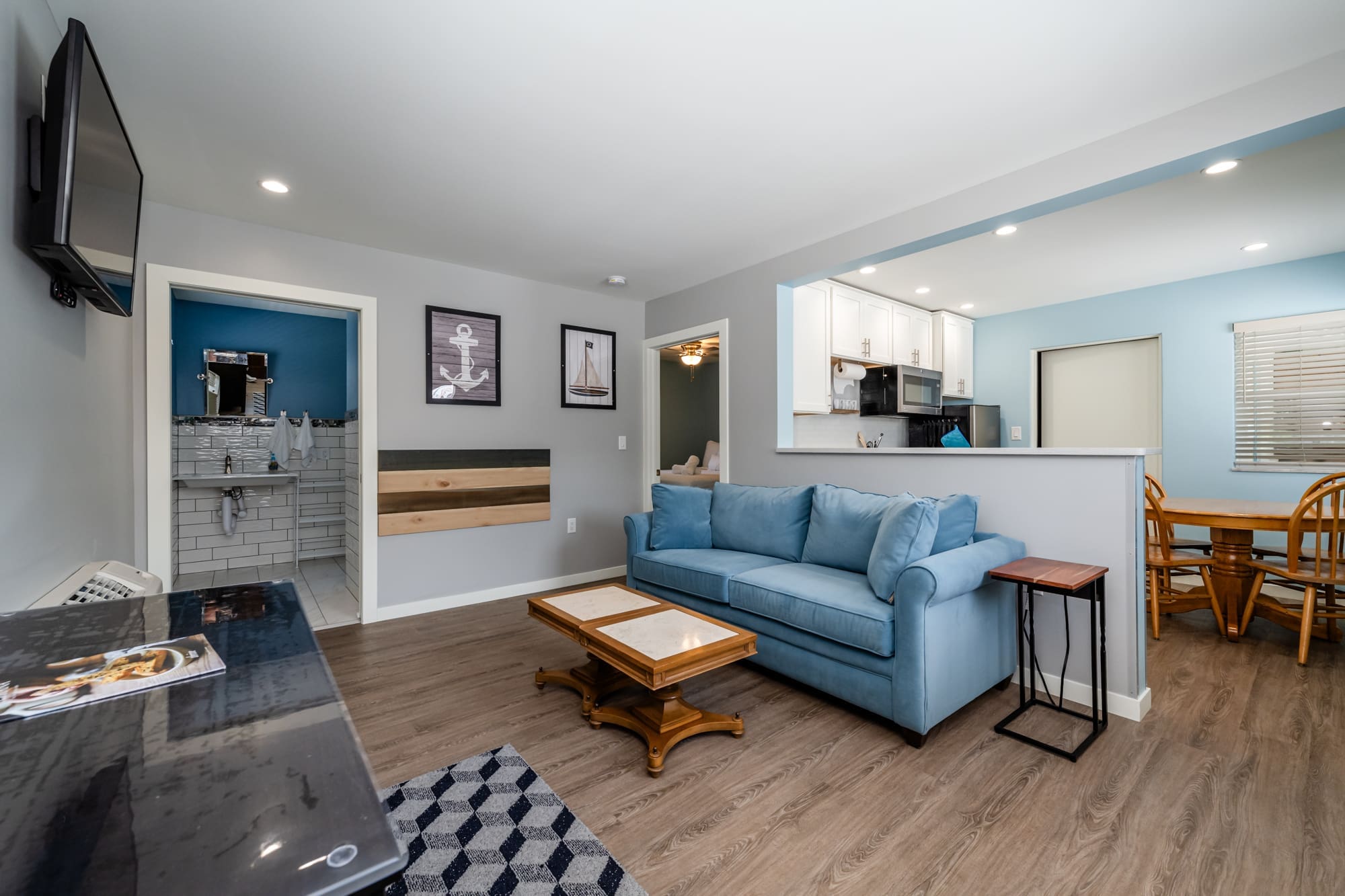 Cozy living area with a blue sofa, nautical-themed wall art, and a view into the kitchen